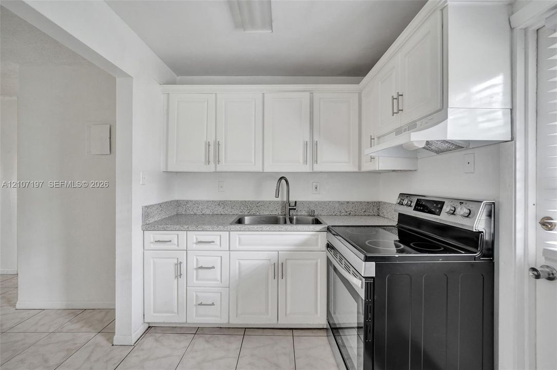 Kitchen featuring white shaker-style cabinetry, stone-finish countertops, stainless steel undermount sink with a gooseneck faucet, black electric range, and tiled flooring