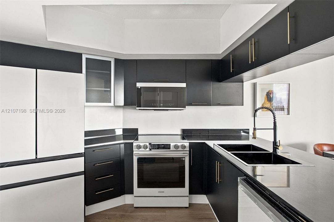 Modern kitchen featuring matte black cabinetry with gold-toned hardware, dark stone countertops, an integrated microwave, a high-arc faucet, and wood-finish flooring