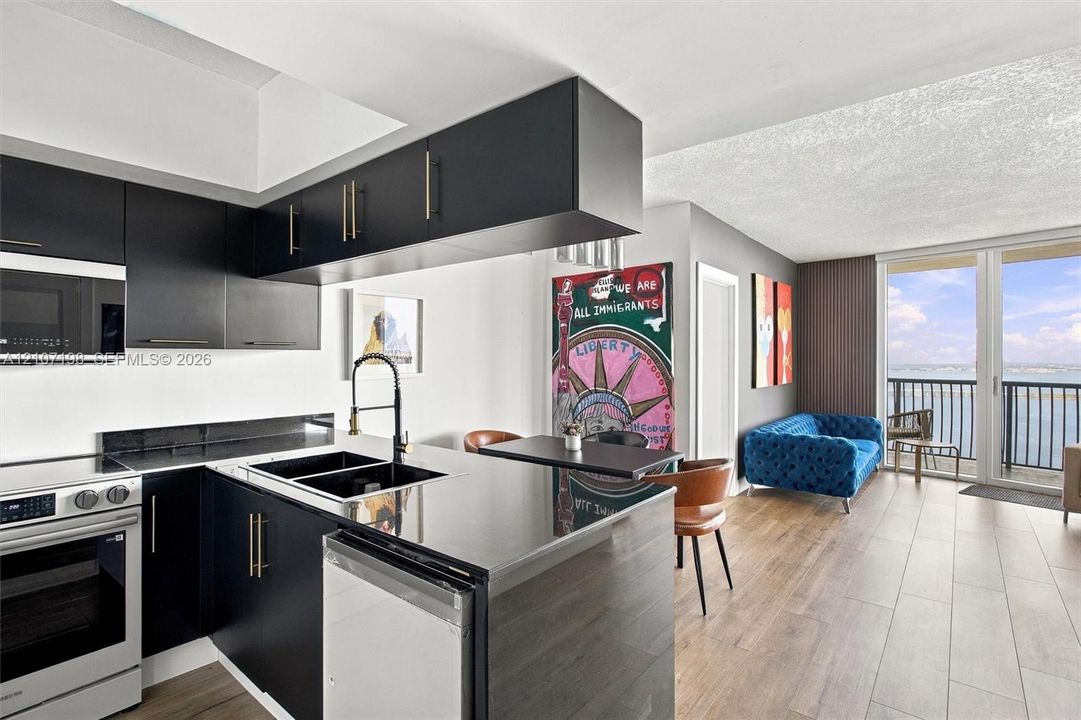 Matte black cabinetry, stone-finish countertops, stainless steel appliance suite, wood-finish flooring, and a private balcony with water backdrop