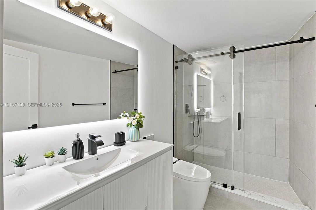 Bathroom featuring a white vanity with an integrated sink, matte black faucet, full-width mirror with integrated lighting, and a glass-enclosed shower with matte black hardware