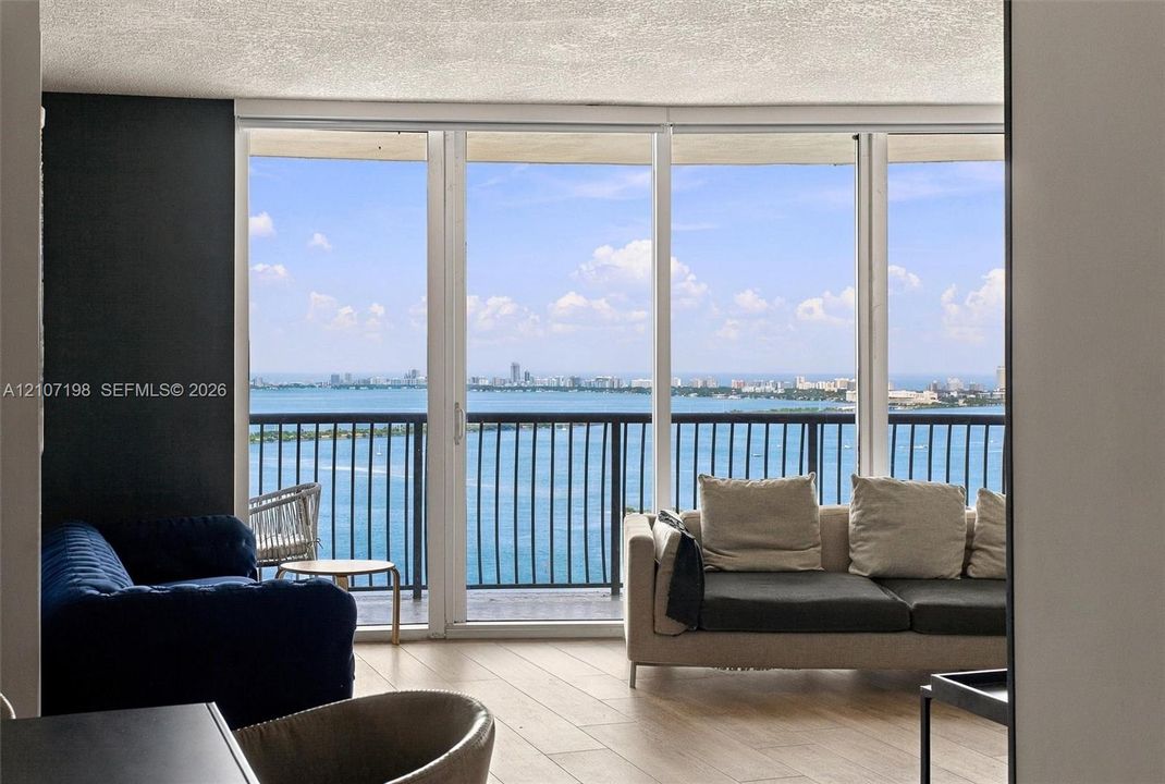 Floor-to-ceiling windows featuring panoramic water and city skyline outlooks, wood-finish flooring, and a private balcony with a metal railing
