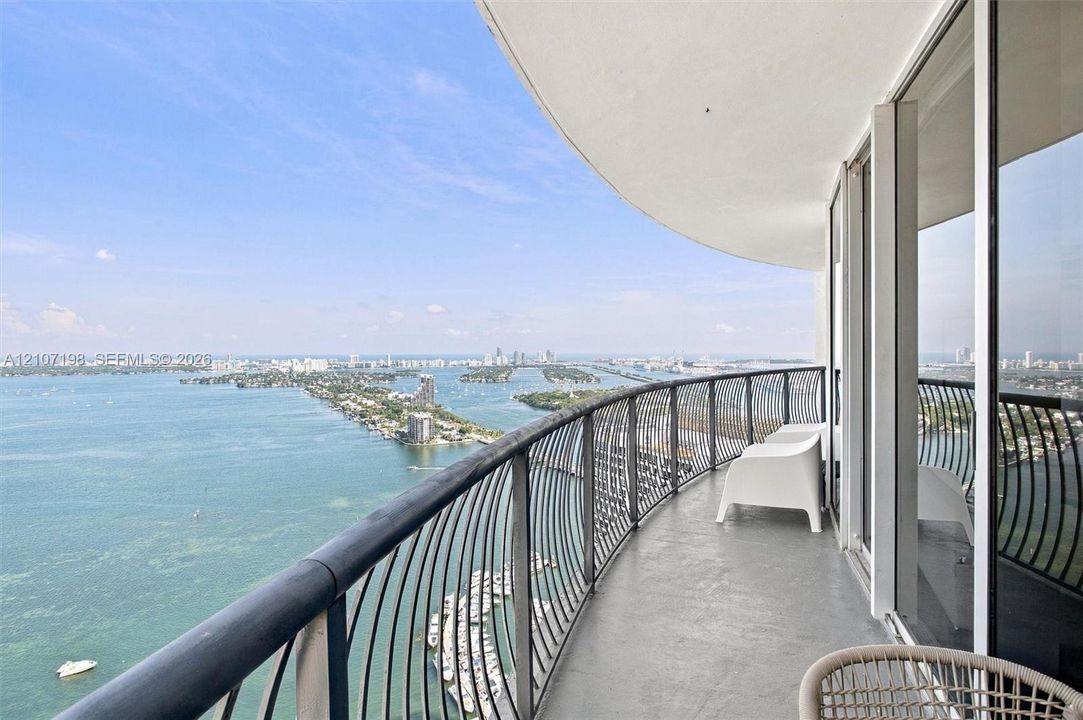 Curved balcony featuring metal railings, concrete flooring, and full-height glass sliding doors