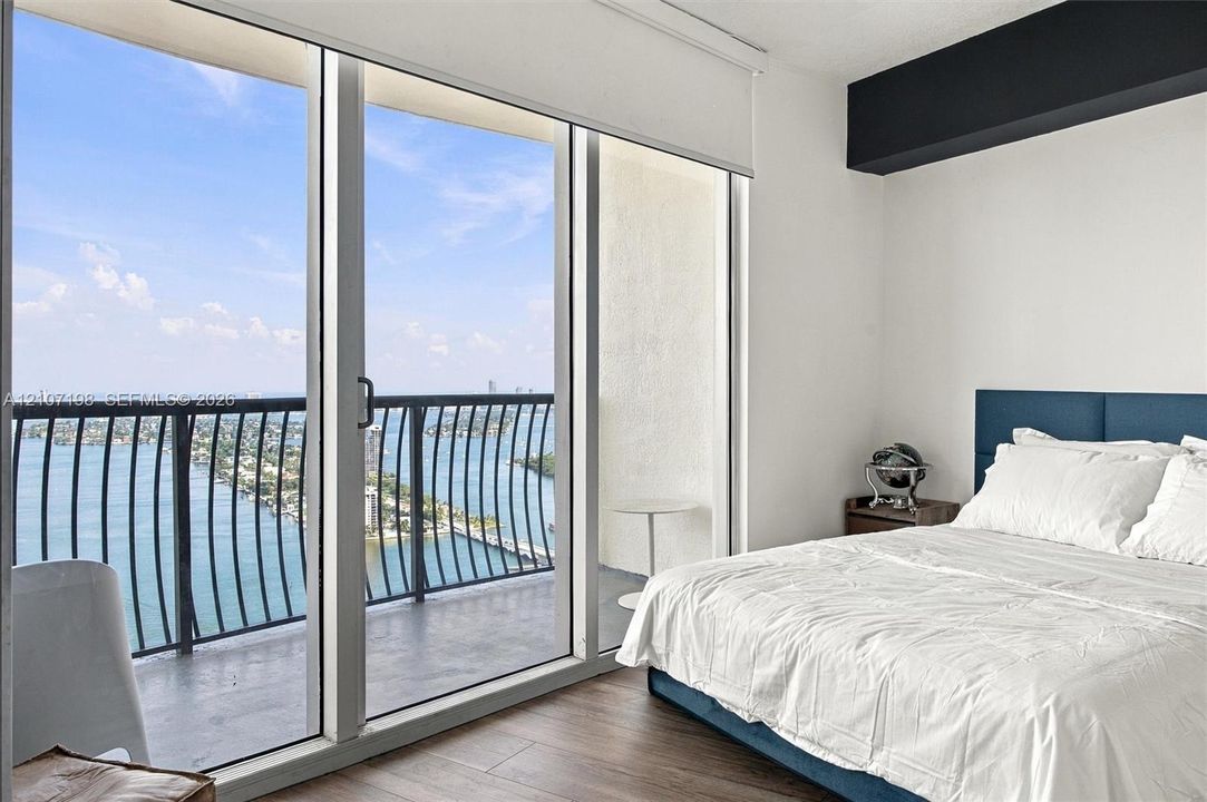 Floor-to-ceiling glass sliding doors, private balcony with metal railing, wood-finish flooring, and recessed ceiling architecture