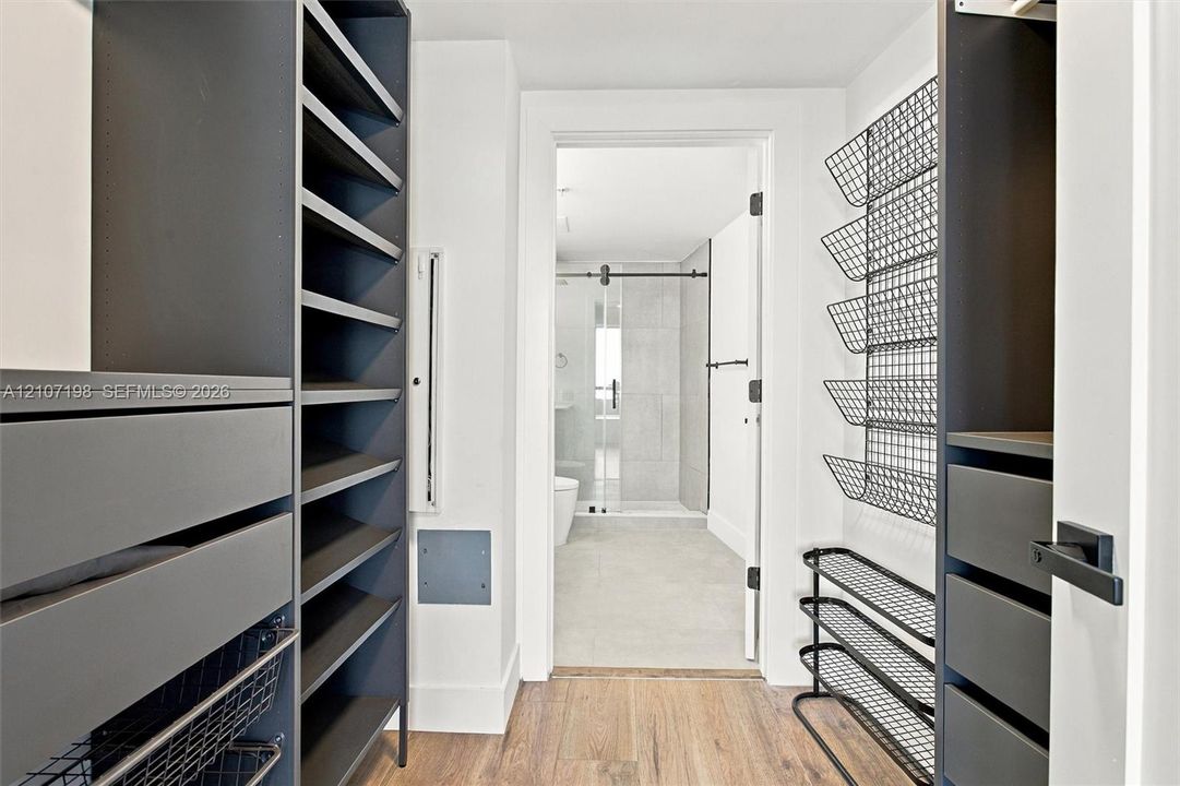 Custom reach-in closet featuring dark-finish built-in cabinetry, integrated drawer banks, adjustable open shelving, and metal wire rack storage with wood-finish flooring
