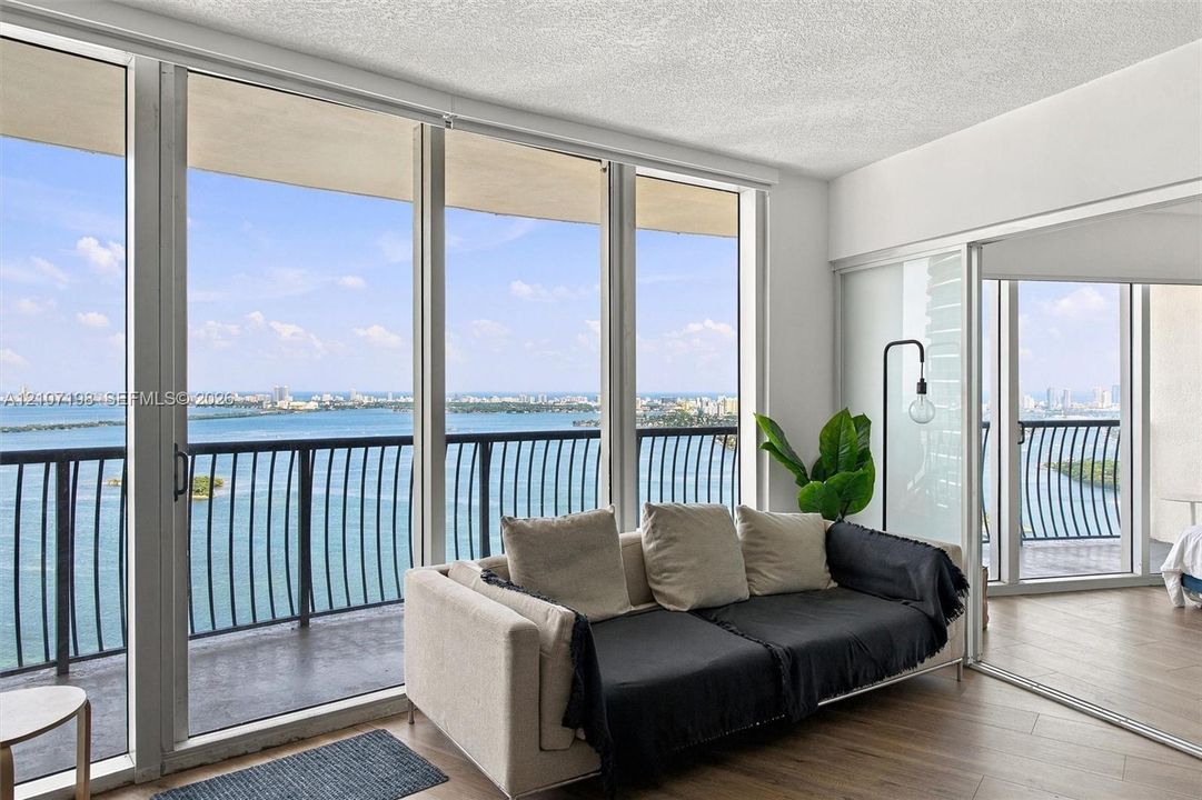 Floor-to-ceiling windows, wood-finish flooring, sliding glass door access to a private balcony, and metal balcony railing