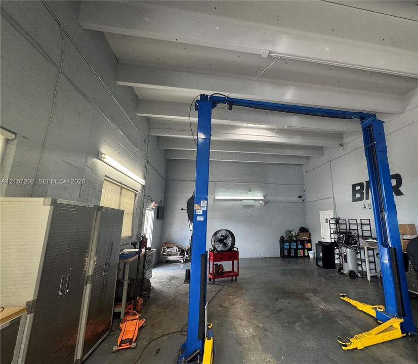 Industrial workspace featuring high ceilings with exposed beams, concrete walls, concrete flooring, and an integrated two-post vehicle lift