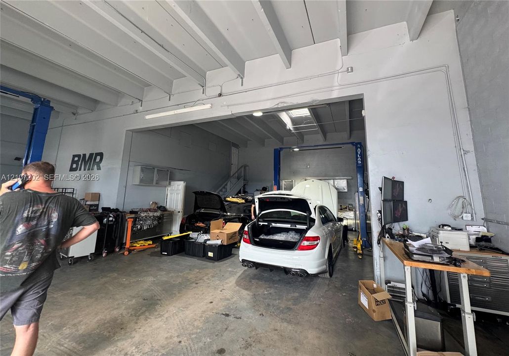 Industrial workspace featuring exposed beam ceilings, concrete flooring, dual vehicle lifts, and high-clearance ceilings