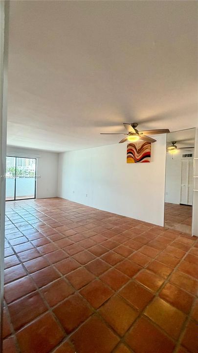 Terra-cotta tile flooring, ceiling fan with integrated lighting, sliding glass door access to exterior, and wall-to-wall mirrored paneling