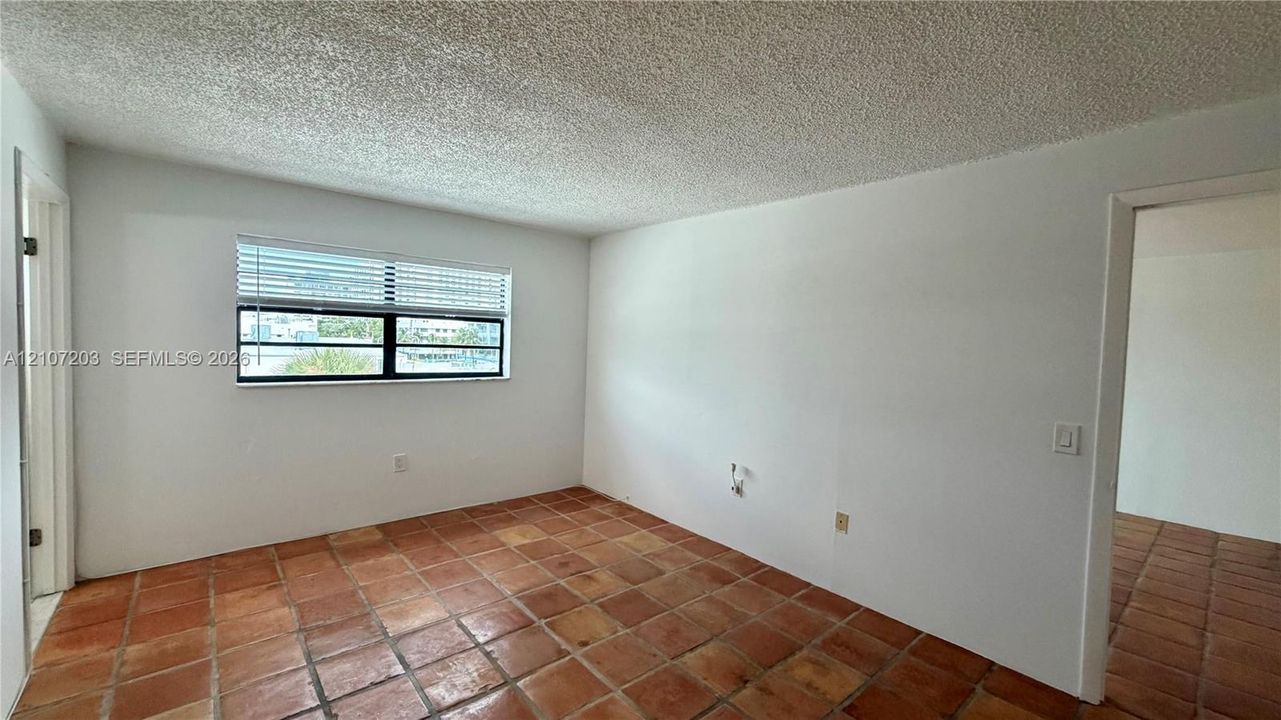 Room featuring square terra-cotta tile flooring, white wall surfaces, and a multi-pane horizontal window with white slatted blinds
