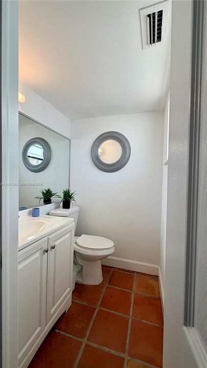 Bathroom featuring terra cotta tile flooring, white cabinetry with an integrated basin, a large wall-mounted mirror, and circular decorative wall accent