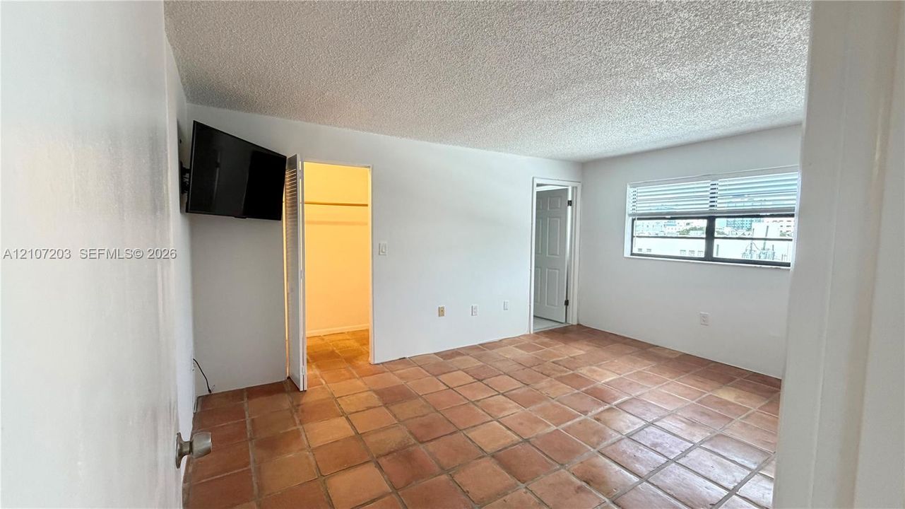 Interior space featuring ceramic tile flooring, textured ceiling, reach-in closet with louvered doors, and window with horizontal blinds
