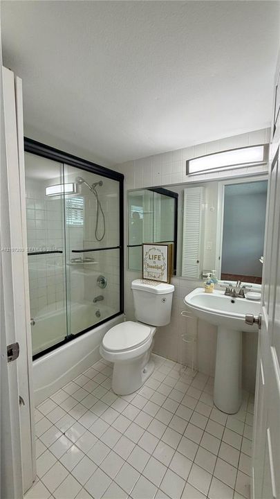 Bathroom featuring a pedestal sink, tub with a glass sliding door enclosure, handheld shower fixture, and square tile flooring