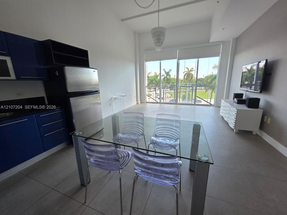 Open-concept floor plan featuring high ceilings, large floor-to-ceiling windows, tile flooring, and custom blue cabinetry with stainless steel appliances