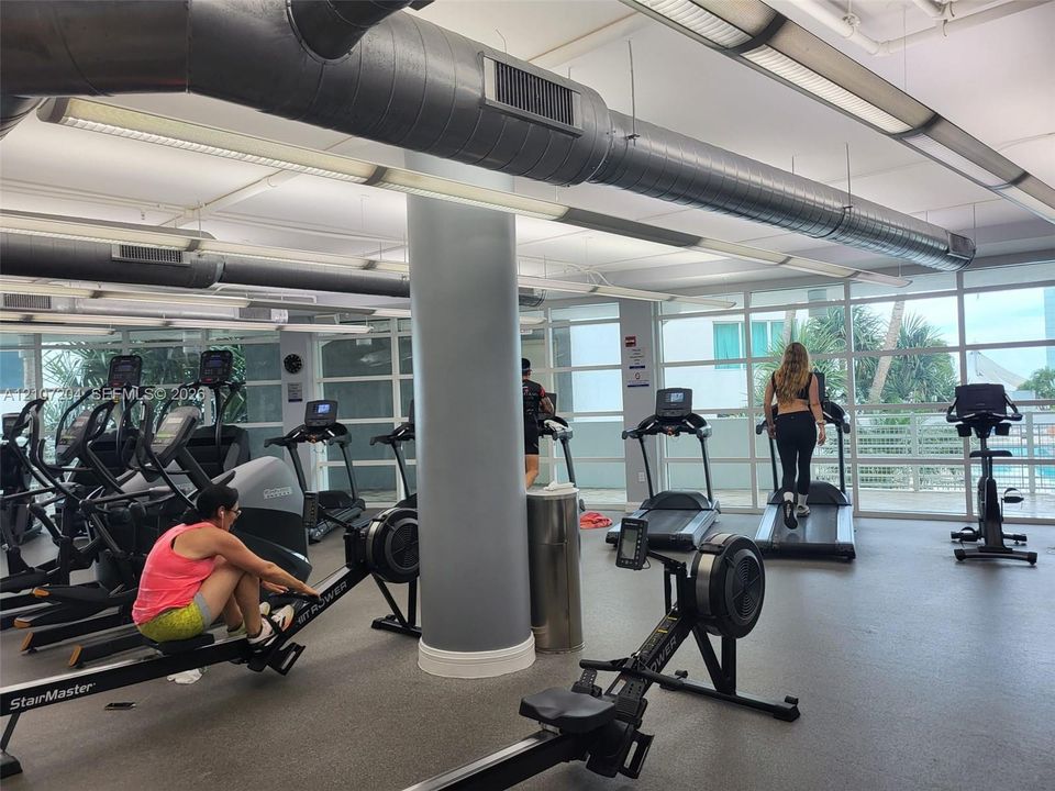 Fitness center featuring industrial-style exposed ductwork, floor-to-ceiling windows, and resilient rubberized flooring