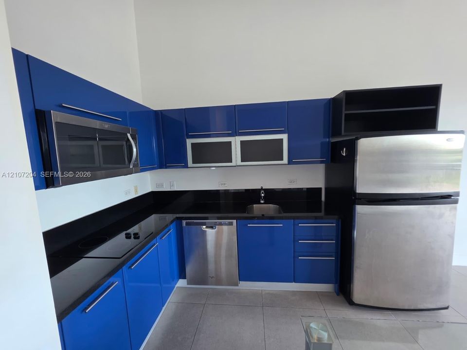Kitchen featuring high-gloss blue cabinetry, black countertops, stainless steel appliances, and large-format tile flooring