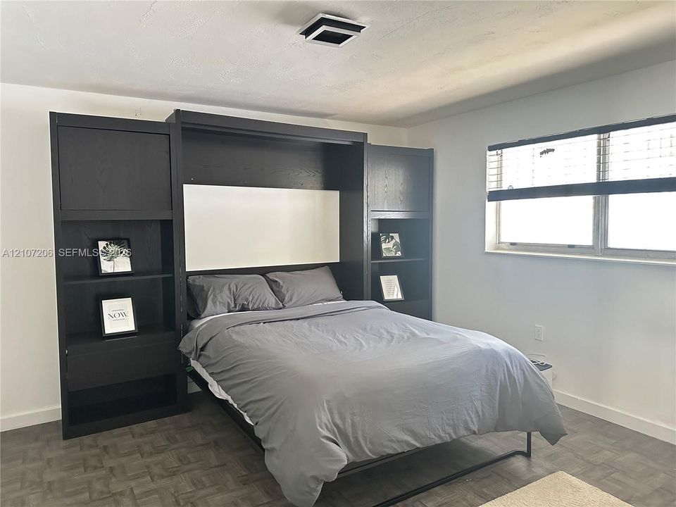 Built-in dark-finish wall unit with integrated shelving, matte-finish window blinds, and square-patterned flooring