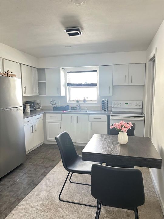 Kitchen featuring white shaker-style cabinetry, stainless steel refrigerator, white electric range, and solid-surface countertops