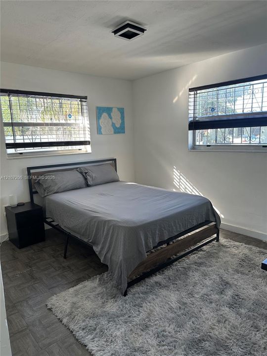 Neutral-toned interior space featuring wood-finish flooring, dual windows with integrated security bars, and a modern square flush-mount ceiling fixture