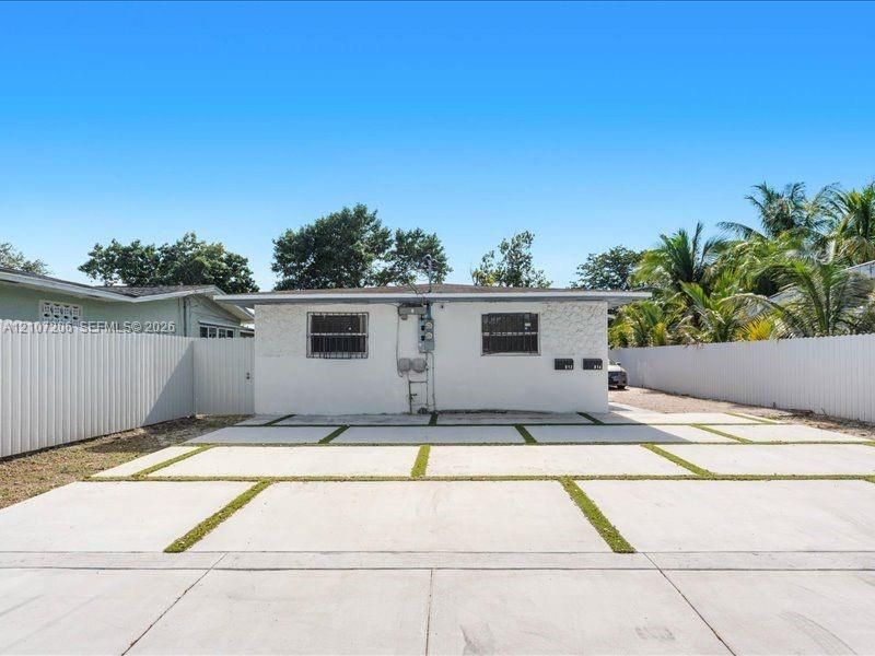 Single-story exterior featuring white stucco siding, a concrete paver driveway with integrated grass ribbons, metal window security bars, and perimeter privacy fencing