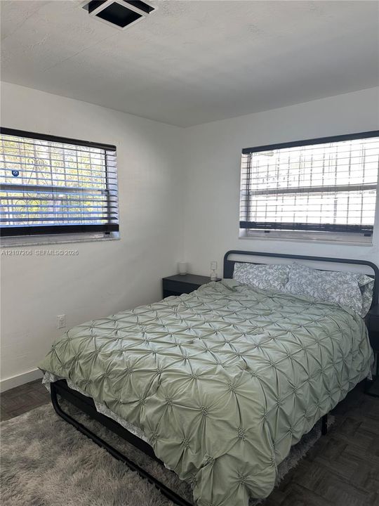 Room featuring two windows with horizontal blinds and wood-finish parquet flooring