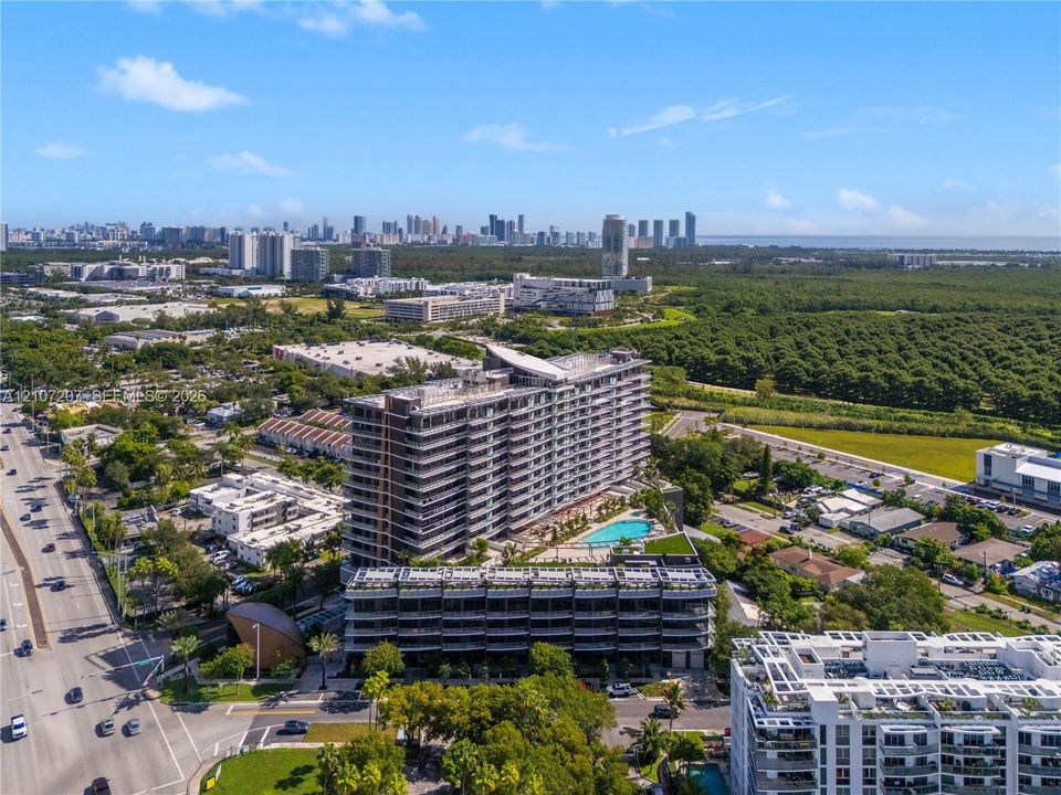 Aerial view of high-rise residential structure featuring an expansive terrace level, outdoor swimming pool, and proximity to expansive natural greenery and urban skyline