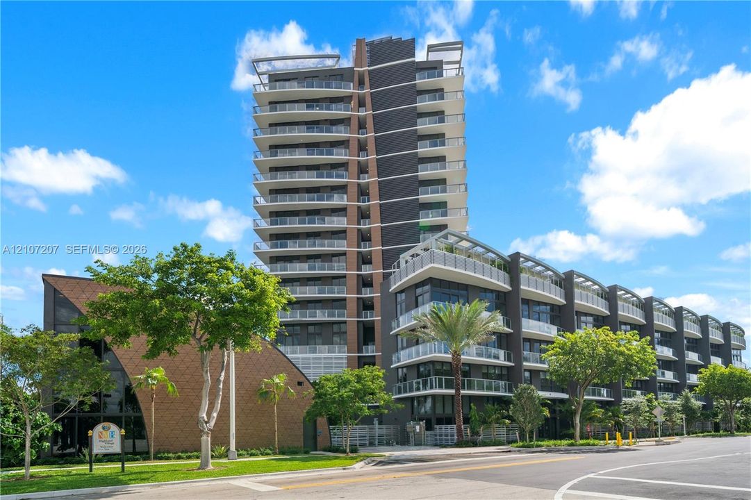 Contemporary high-rise architecture featuring glass-railed private balconies, a multi-story facade with dark paneling, and an attached low-rise structure with textured shingle-style exterior cladding