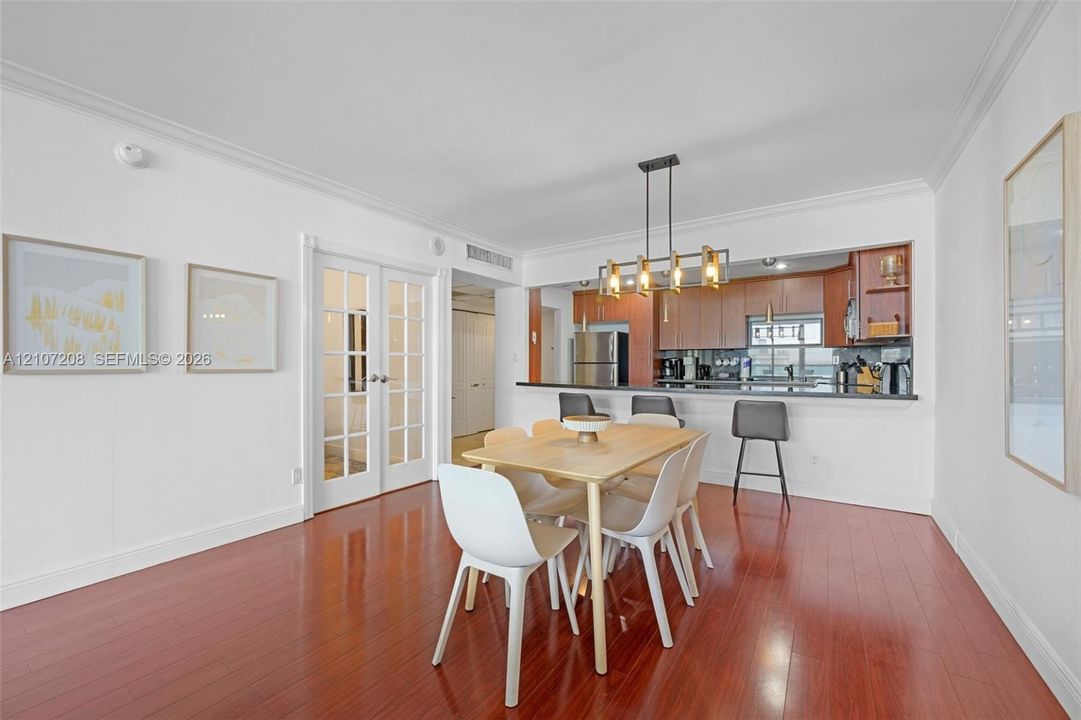 Dining area featuring wood-finish flooring, crown molding, multi-pane French doors, and a linear multi-light chandelier