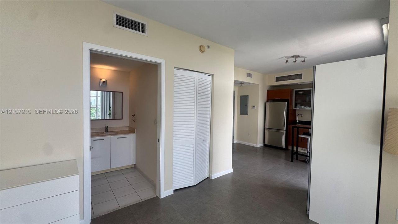 Interior space featuring large-format tile flooring, a kitchenette equipped with stainless steel appliances and cabinetry, and a bathroom containing a vanity with a solid-surface countertop and wall-mounted mirror