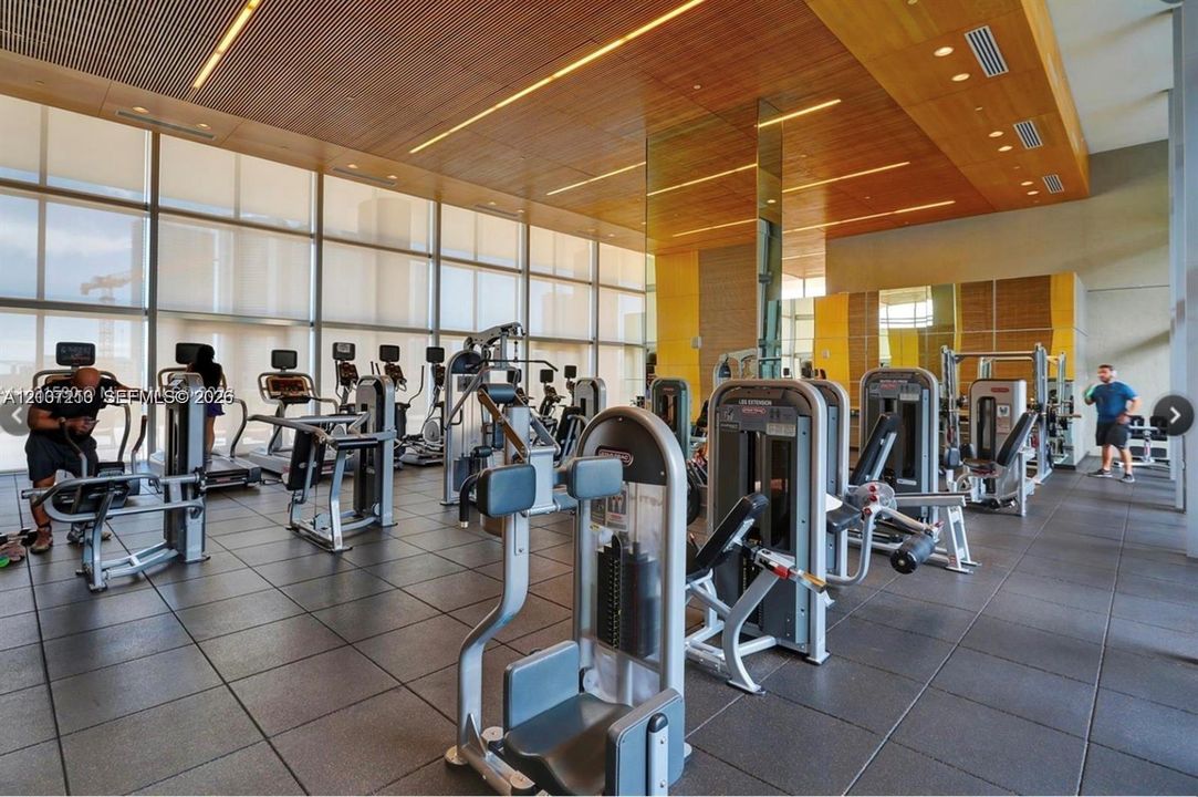 Fitness center featuring floor-to-ceiling windows, slatted wood-finish ceiling, linear recessed lighting, and large-format tile flooring