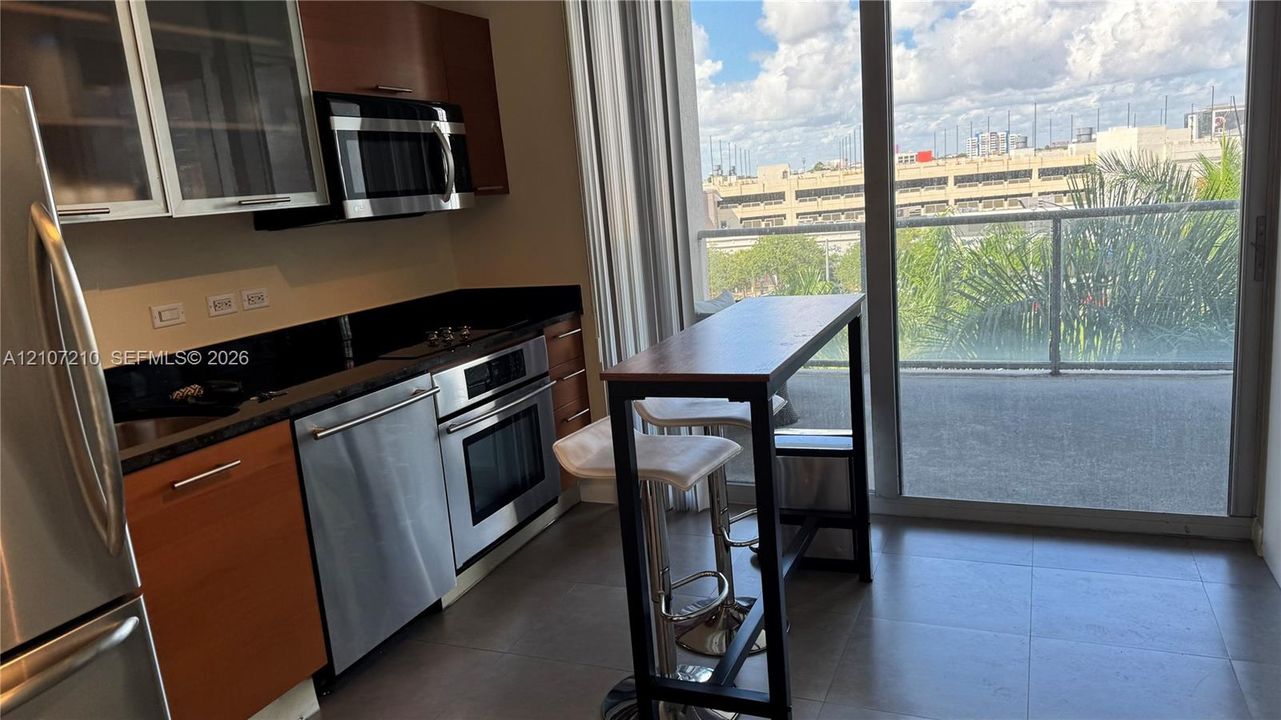 Kitchen featuring stainless steel appliances, flat-panel cabinetry, stone countertops, large-format tile flooring, and floor-to-ceiling sliding glass doors opening to a balcony