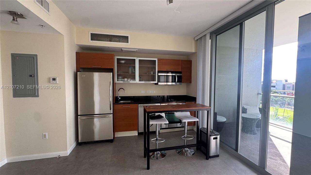 Kitchen featuring wood-veneer cabinetry, dark stone countertops, stainless steel appliances, and tile flooring, including full-height sliding glass doors