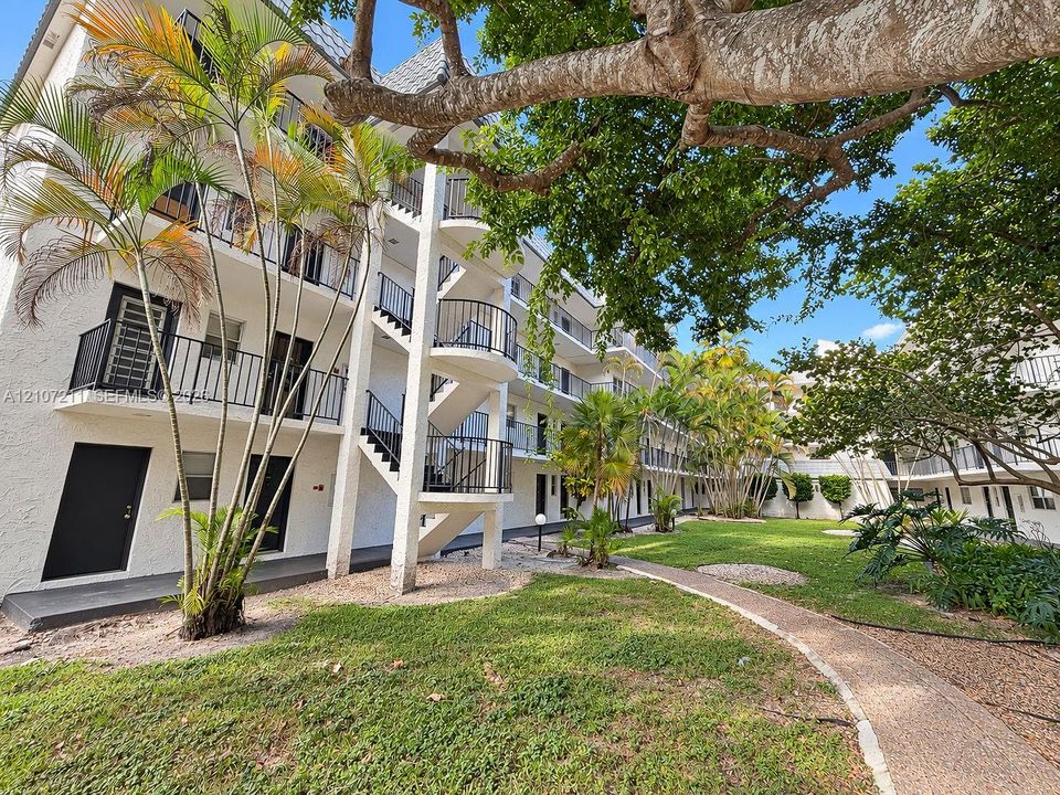Multi-story exterior featuring white textured stucco facade, spiral staircases, black metal railings, paved walkways, and mature landscaping
