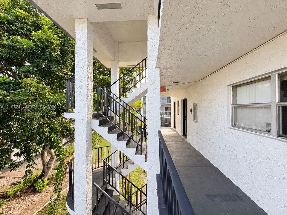 Exterior walkway featuring a stucco facade, metal railings, and a concrete-surfaced landing