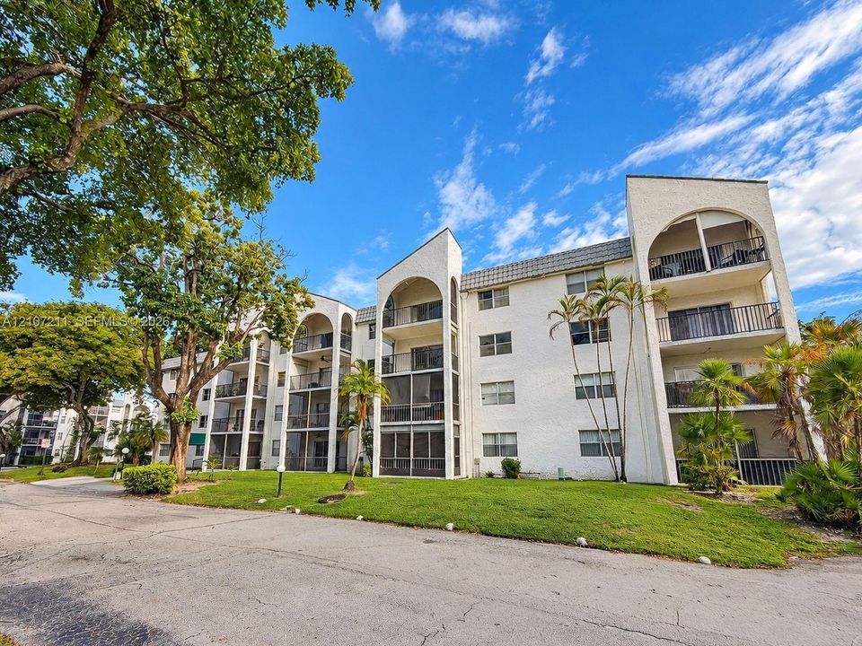 Multi-story stucco exterior featuring arched balconies, screened-in lanais, mature trees, and landscaped grounds