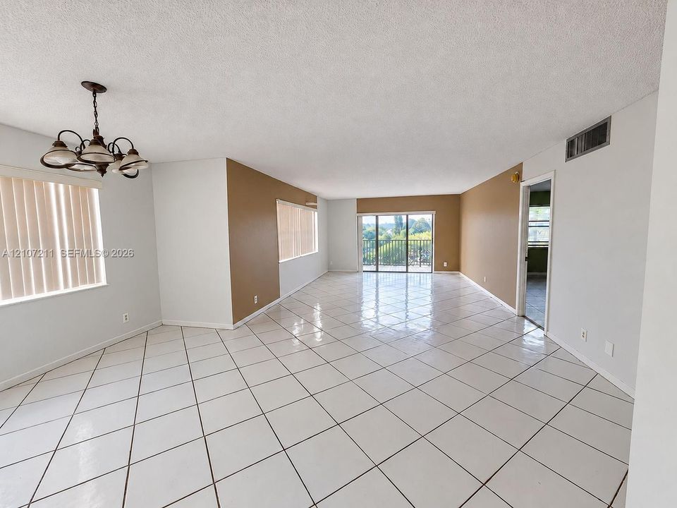 “Spacious room featuring white ceramic tile. Wall paint digitally enhanced using AI.”flooring, neutral wall tones, a multi-arm chandelier, and sliding glass doors leading to a balcony