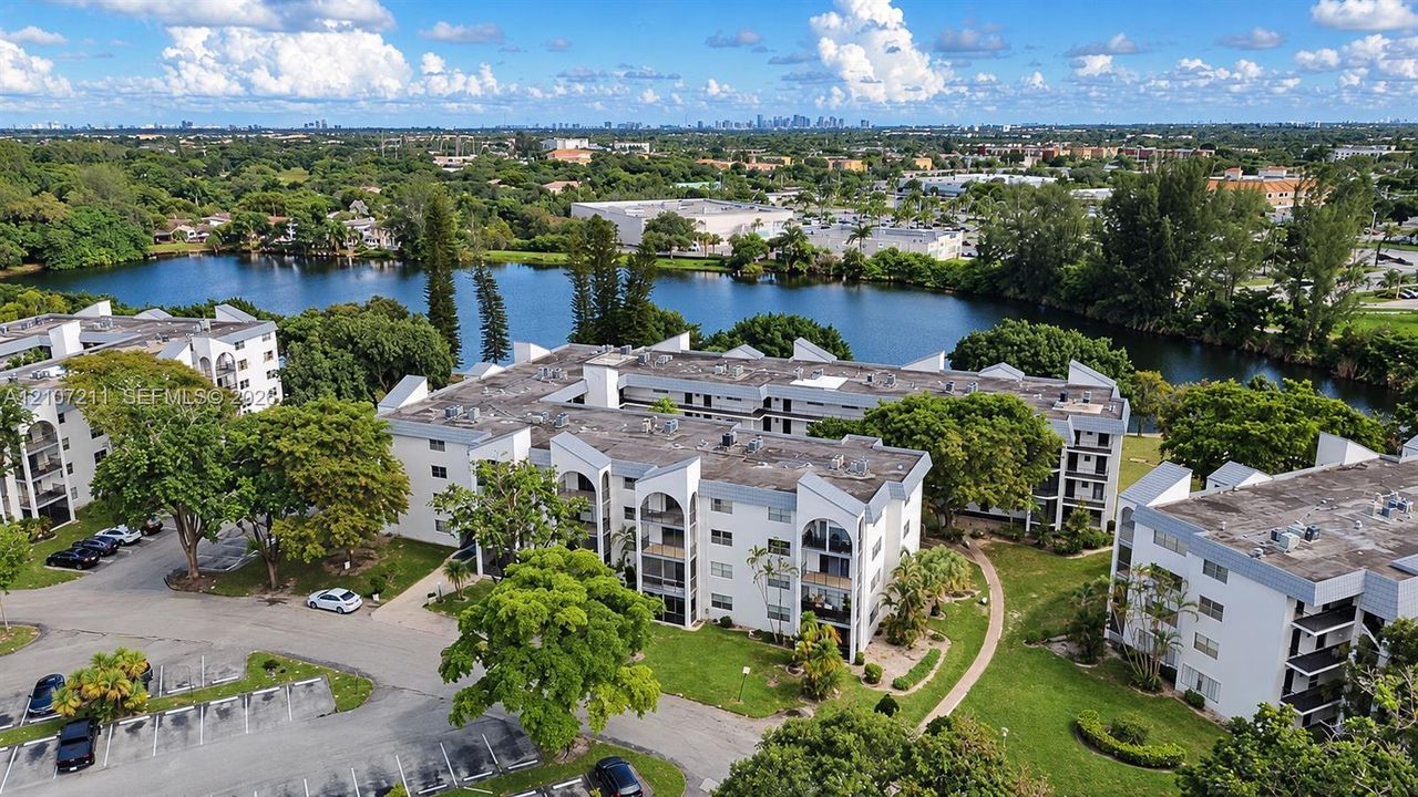 Multi-story residential complex featuring arched architectural details, private balconies, paved surface parking, and manicured grounds situated along a waterfront
