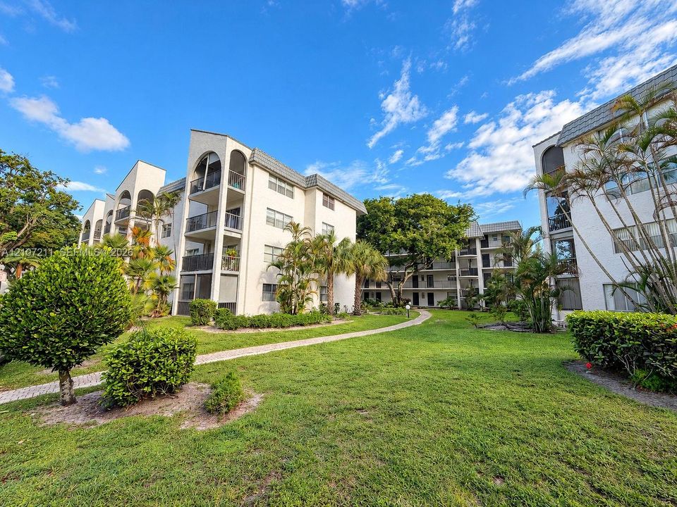 Multi-story exterior featuring arched architectural detailing, private balconies with metal railings, a paved pedestrian pathway, and mature landscaping