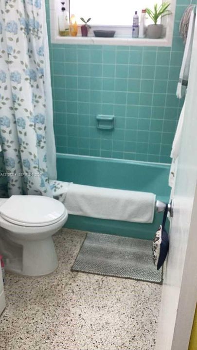 Bathroom featuring a bathtub with matching tile surround, recessed soap dish, terrazzo flooring, and window