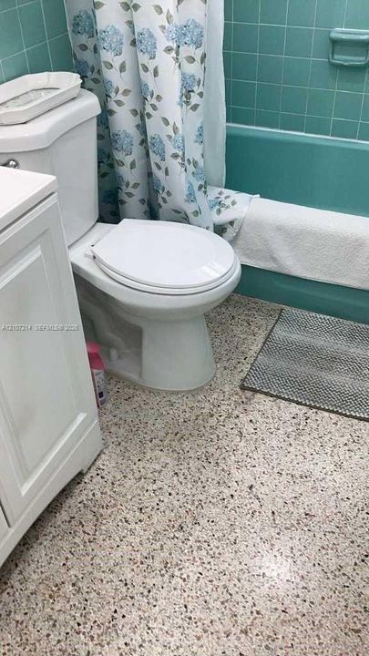 Bathroom featuring white cabinetry, integrated porcelain toilet, built-in recessed soap dish, and terrazzo-style flooring