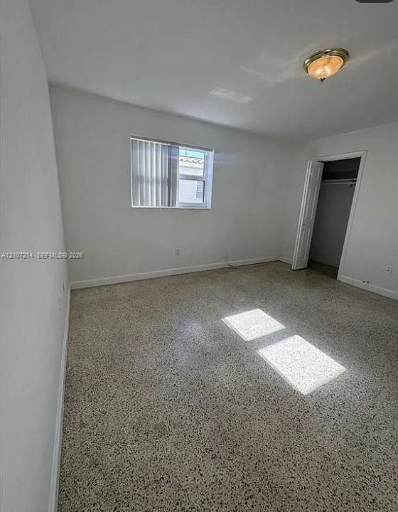 Neutral-toned room featuring terrazzo flooring, a single-pane window with vertical blinds, a flush-mount ceiling light fixture, and a built-in closet with double doors
