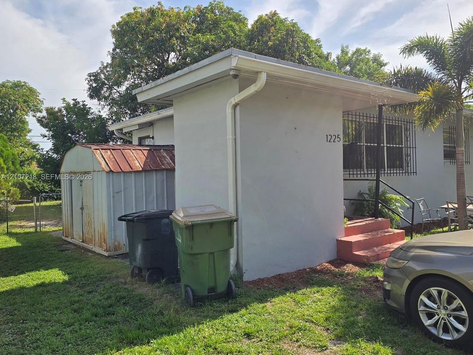 Stucco exterior featuring metal window security bars, concrete entry steps with metal handrails, and a detached metal storage shed