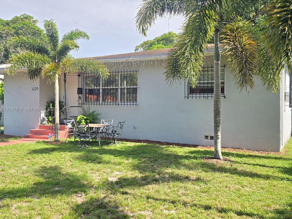Exterior facade featuring stucco siding, metal window security bars, a concrete front entry, and mature palm trees