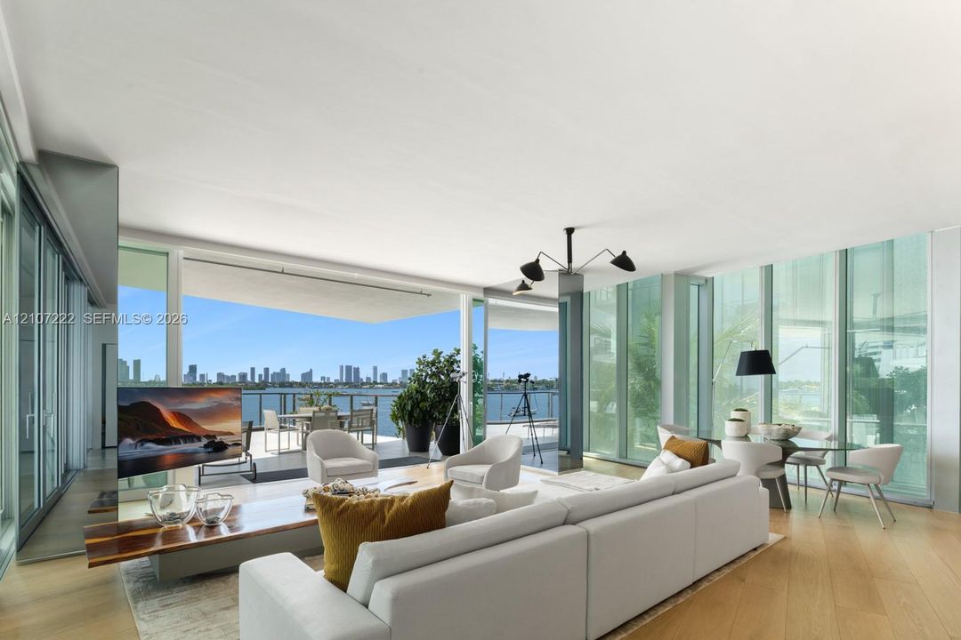 Floor-to-ceiling glass walls, wood-finish flooring, expansive covered balcony, and modern multi-arm ceiling fixture