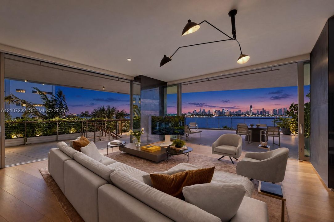 Open-concept living space featuring wood-finish flooring, expansive floor-to-ceiling glass sliding doors, a recessed balcony, and a multi-arm architectural pendant light