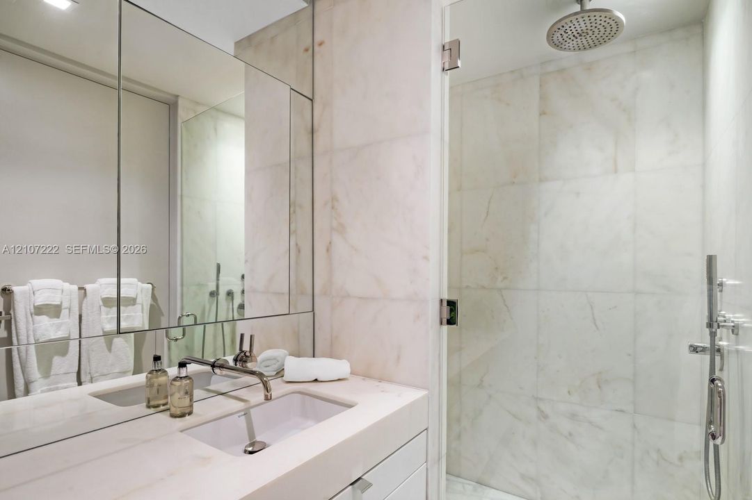 Bathroom featuring a floating vanity with a stone countertop and integrated sink, full-height wall mirror, stone-tile walk-in shower with a glass door, rainfall showerhead, and a hand-held shower sprayer