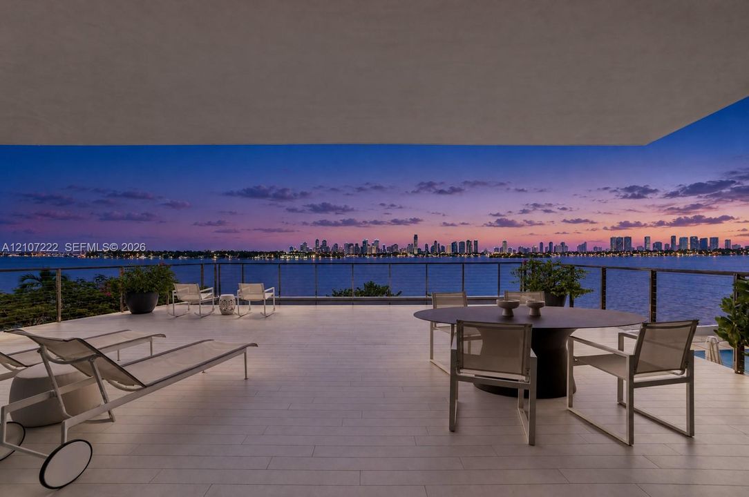 Covered terrace featuring light-toned tile flooring, a glass-panel railing, and panoramic water and city skyline backdrop