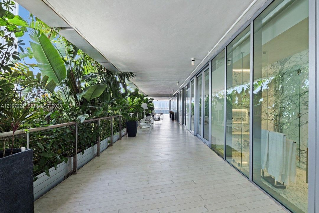 Expansive covered terrace featuring light-toned tile flooring, floor-to-ceiling glass panel walls, integrated railing, and built-in landscape planters