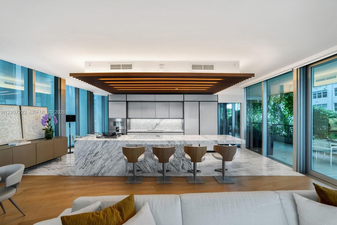 Kitchen featuring an expansive stone-topped island with integrated seating, stone flooring, floor-to-ceiling glass panel walls, and custom wood-slat ceiling detail