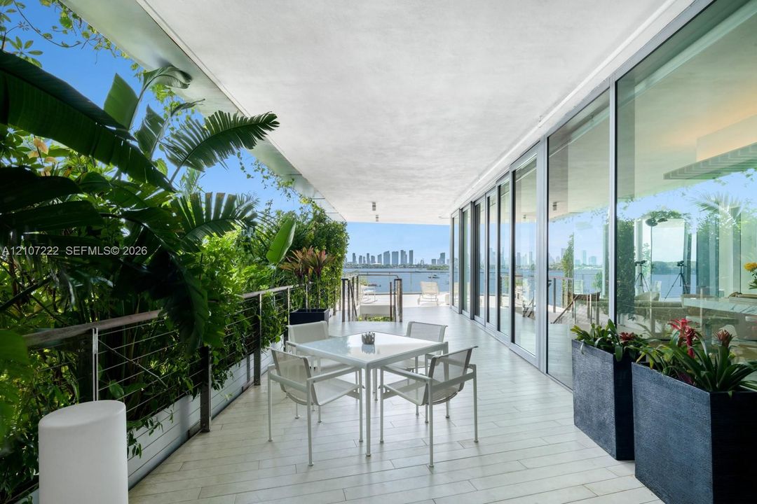 Covered outdoor terrace featuring light-toned tile flooring, floor-to-ceiling glass panel walls, a stainless steel cable railing system, and integrated built-in planters