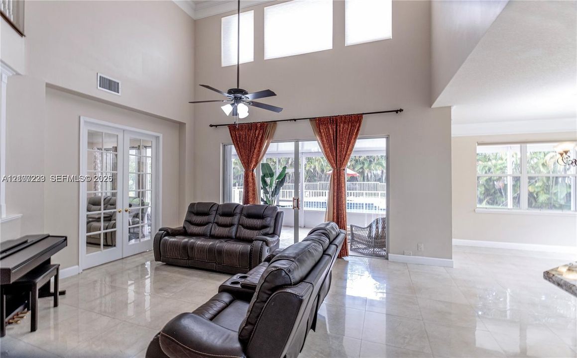High-ceilinged room featuring neutral tile flooring, clerestory windows, a dual-pane sliding glass door, and white-trimmed French doors